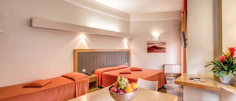 A hotel room with two single beds, a wooden table with a fruit bowl, a small dining table, and a chair.