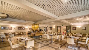 Un comedor amplio con varias mesas y sillas, una estación de buffet central y un techo con diseño de cuadrícula.