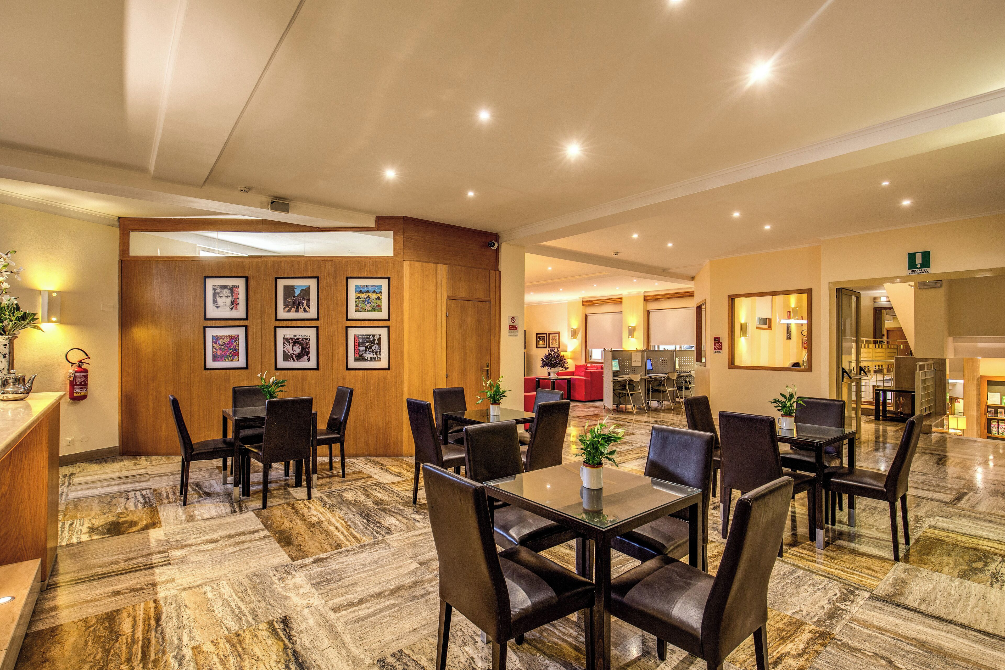 Un hall d’hôtel avec un sol en marbre, plusieurs tables à manger entourées de chaises, un comptoir de réception et des tableaux encadrés accrochés au mur.