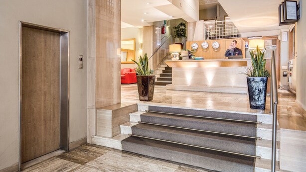 Un vestíbulo de hotel con mostrador de recepción, una escalera y una recepcionista.