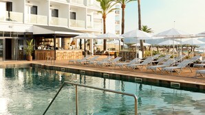 Un área de piscina con sillas de descanso y sombrillas, un bar y un edificio con balcones.