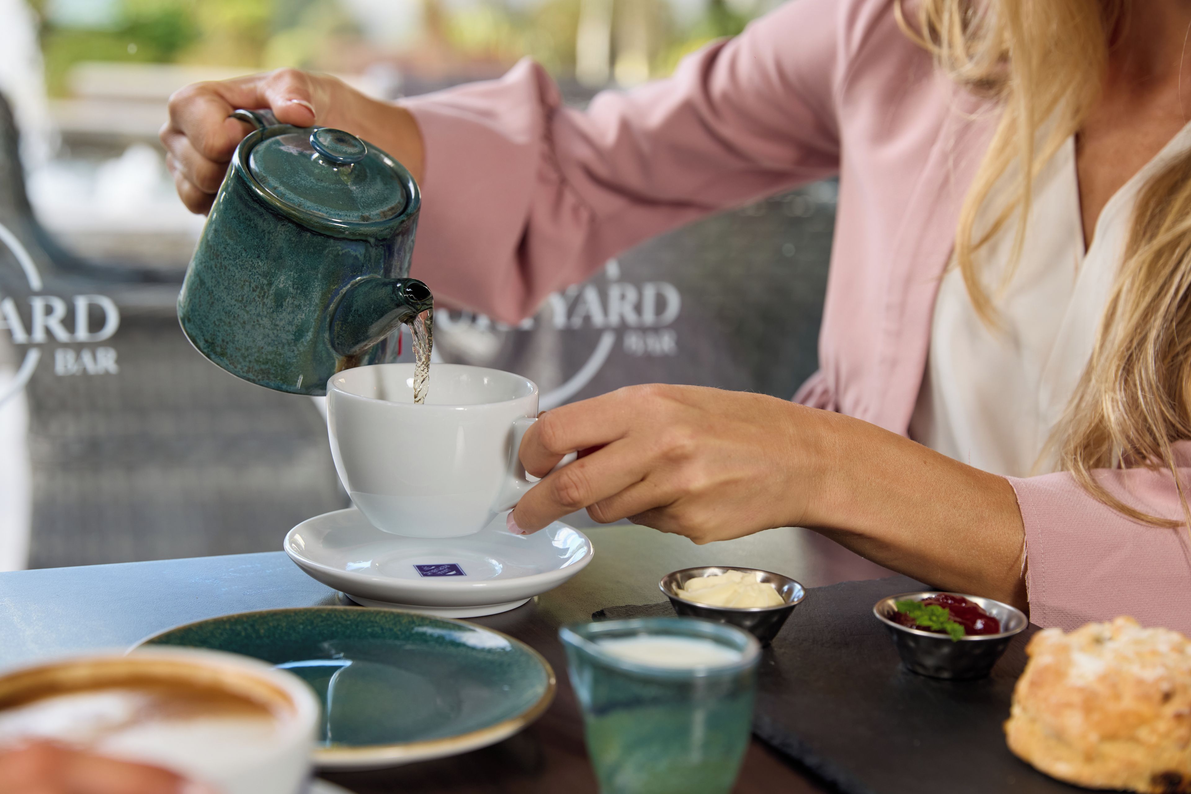 A person pouring a beverage into a cup at a table with a sign that reads 'CARD BAR'.