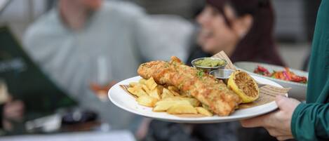 A person holding a plate with fish, chips, and a small bowl of sauce.
