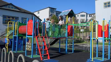 Un parque infantil con diversas estructuras de juego, como toboganes y zonas de escalada, rodeado por una valla.