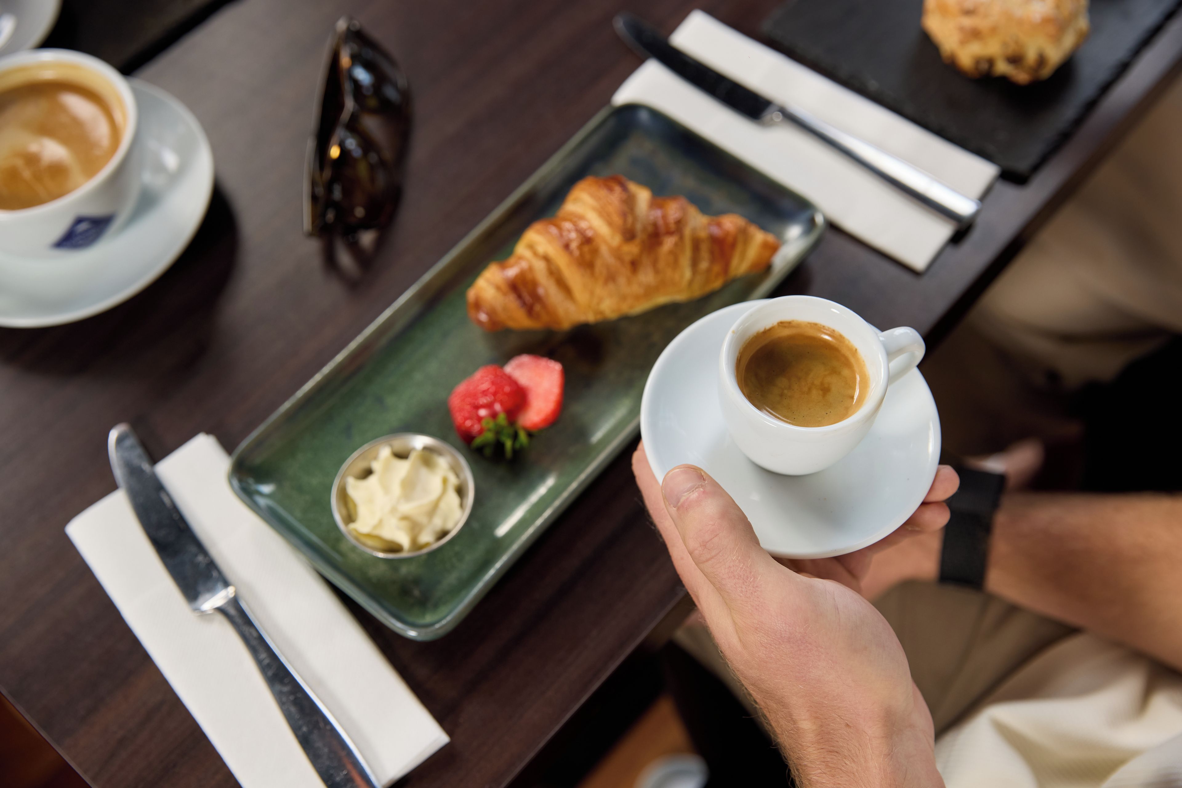 Une table avec un croissant, une fraise et une tasse de café.