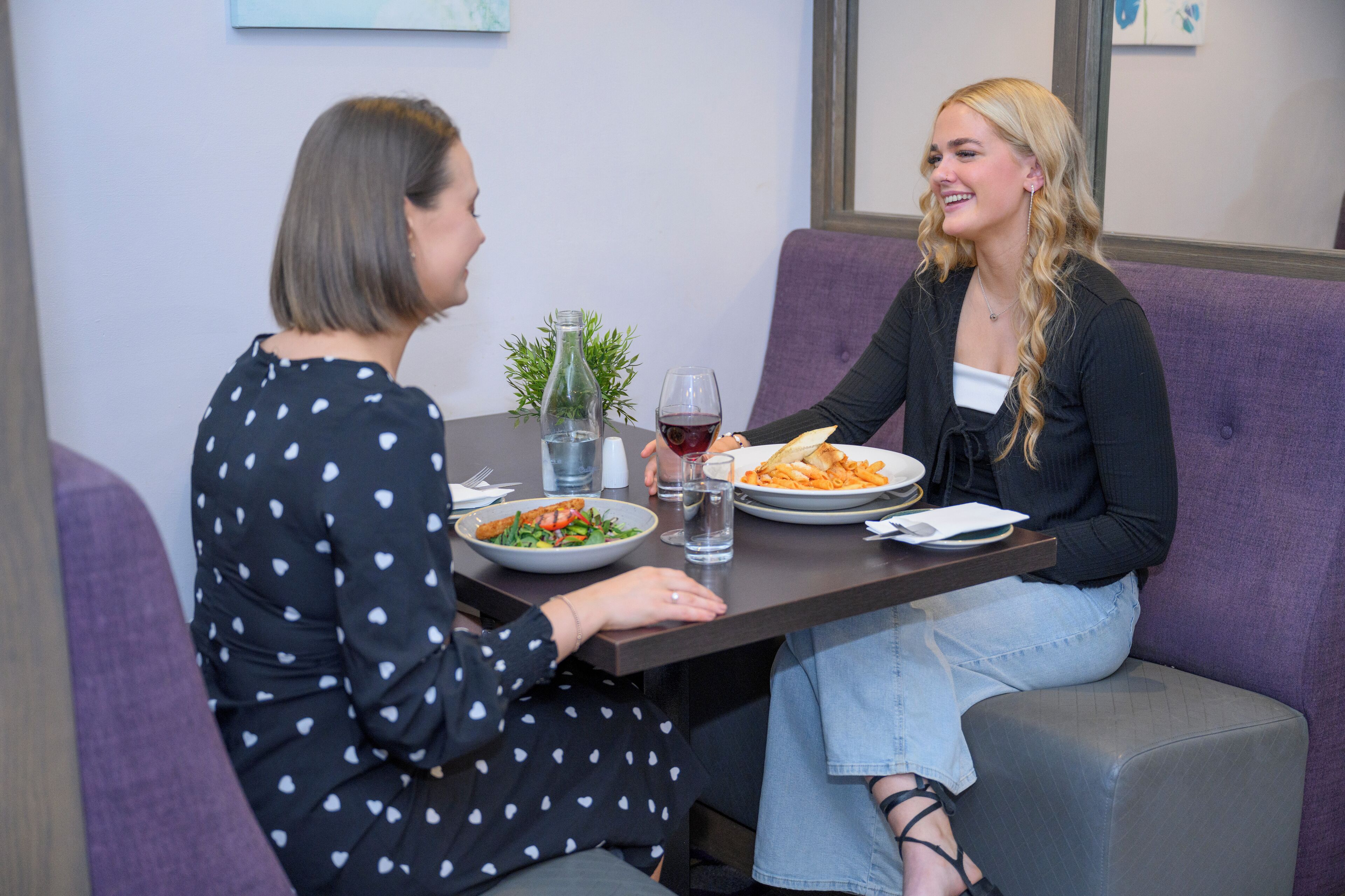 Two people seated at a table with plates of food, a bottle of water, and a glass of red wine.