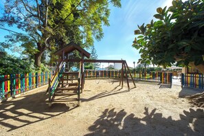 A playground with a swing set and climbing structure, surrounded by a colorful fence. - Globales Gardenia (Fuengirola)