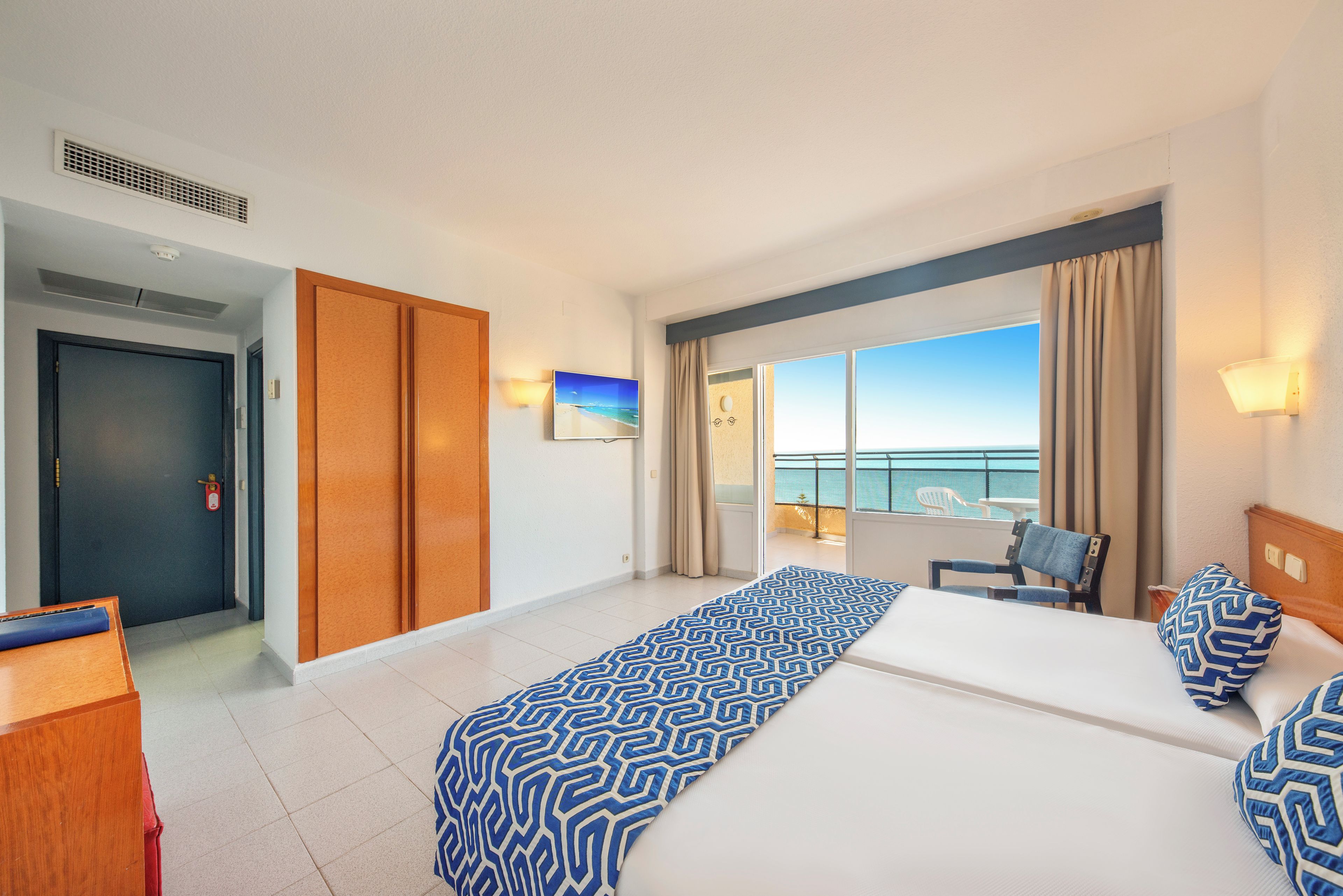 A hotel room with a balcony, a bed, a desk, and a wardrobe.