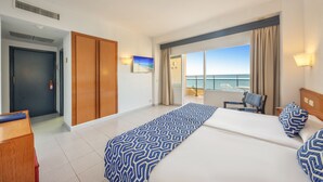 A hotel room with two beds, a view of the sea, a balcony with a chair, and a wooden wardrobe. - Globales Gardenia (Fuengirola)