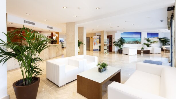 A modern hotel lobby with white sofas, a large potted plant, and a view of the ocean through the windows. - Globales Gardenia (Fuengirola)