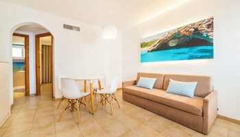 Una sala de estar moderna con un sofá color beige, sillas blancas, una mesa de comedor y un cuadro grande de una escena costera.