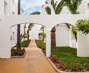 A pathway flanked by white walls and arches, leading to a building with a visible entrance.