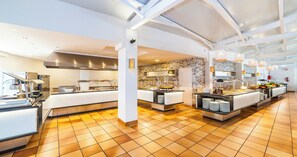 A spacious hotel kitchen with modern appliances, a stone wall, and a buffet area. - Globales Aparthotel Bouganvilla (Sant Llorenc des Cardassar)