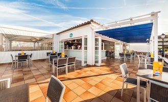 Un área de café al aire libre con mesas, sillas, una barra y una zona de estar cubierta.