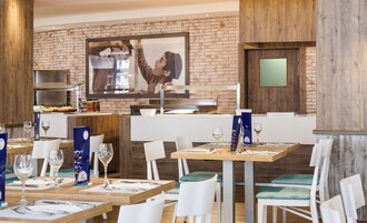 Un restaurante con paredes de ladrillo, detalles de madera y un cuadro grande enmarcado. Las mesas están dispuestas con copas de vino y menús.
