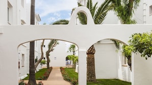 A pathway flanked by white walls and arches, leading to a building with windows and a sign. - Globales Aparthotel Bouganvilla (Sant Llorenc des Cardassar)