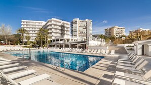Un área de piscina con sillones de descanso, una piscina y edificios modernos al fondo.