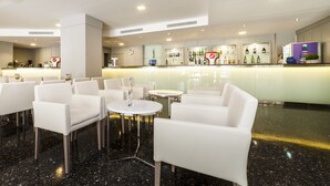 Un vestíbulo de hotel con sillas de cuero blanco, mostrador de recepción y una zona de bar con botellas.