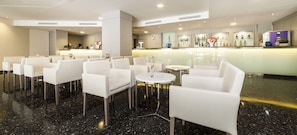 A hotel lobby with white leather chairs, a reception desk, and a bar area with bottles. - Globales Palmanova (Calvia)