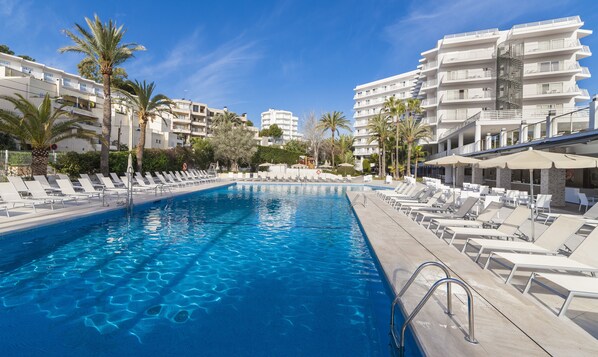 Una piscina con sillas de descanso y sombrillas, rodeada de palmeras y edificios modernos.