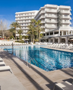 Una piscina con sillones de descanso y un edificio de hotel de varios pisos al fondo.