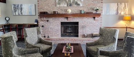 A living room with a brick fireplace, floral-patterned chairs, a coffee table, and artwork on the walls.