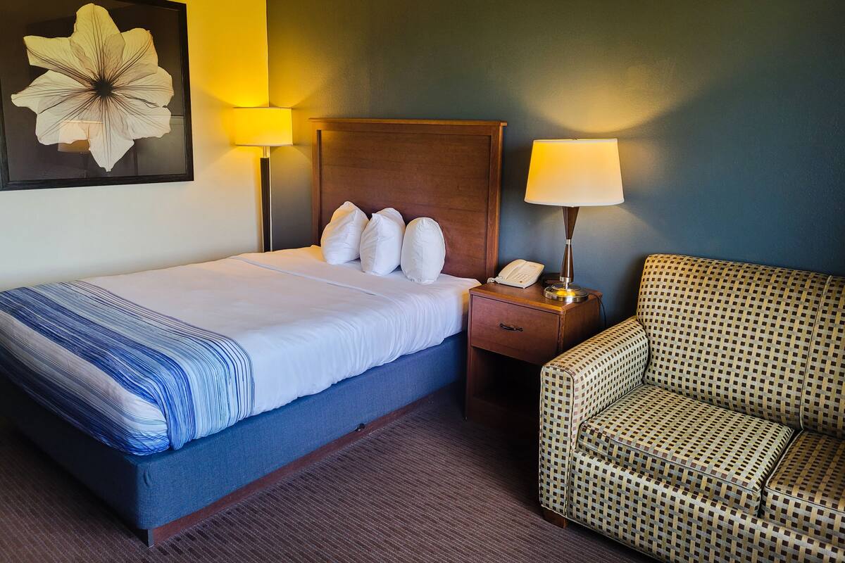 Ein Hotelzimmer mit einem Bett, einem Nachttisch mit Lampe, einem Telefon und einem gemusterten Sessel.