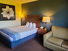 Una habitación de hotel con una cama, una mesita de noche con lámpara, un teléfono y un sillón estampado.