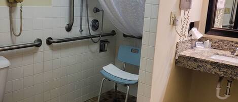 Un baño con inodoro, barras de apoyo, ducha con cortina, lavabo con espejo y cubo de basura.