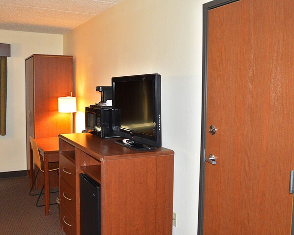 A compact hotel room with a kitchenette, a television, a lamp, and a wooden wardrobe.