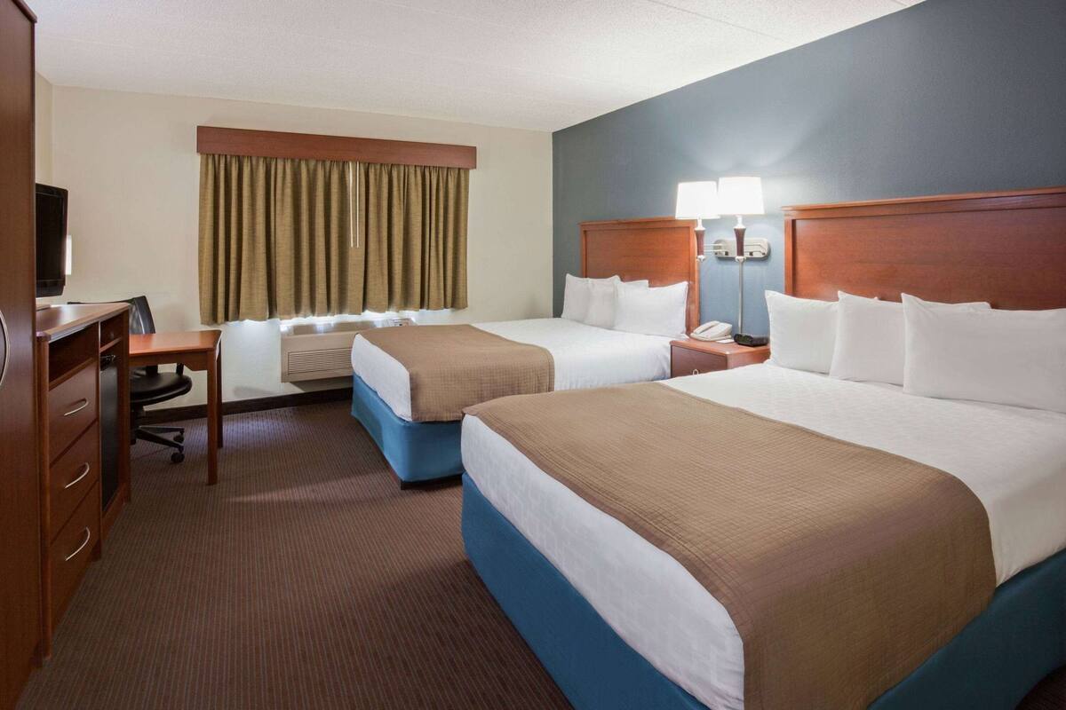 Ein Hotelzimmer mit zwei Betten, einem Schreibtisch, einem Stuhl, einem Fernseher und einem Fenster mit Vorhängen.