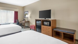 Quarto de hotel com duas camas, uma escrivaninha com cadeira, televisão, micro-ondas e um pequeno banco.
