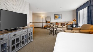 Quarto de hotel com uma cama grande, televisão, escrivaninha com cadeira, mesinha e um sofá.