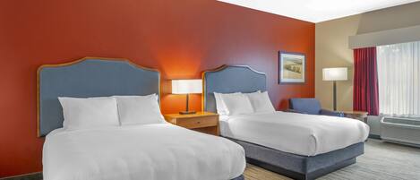 A hotel room with two beds, a nightstand, a lamp, a chair, and a window with curtains.