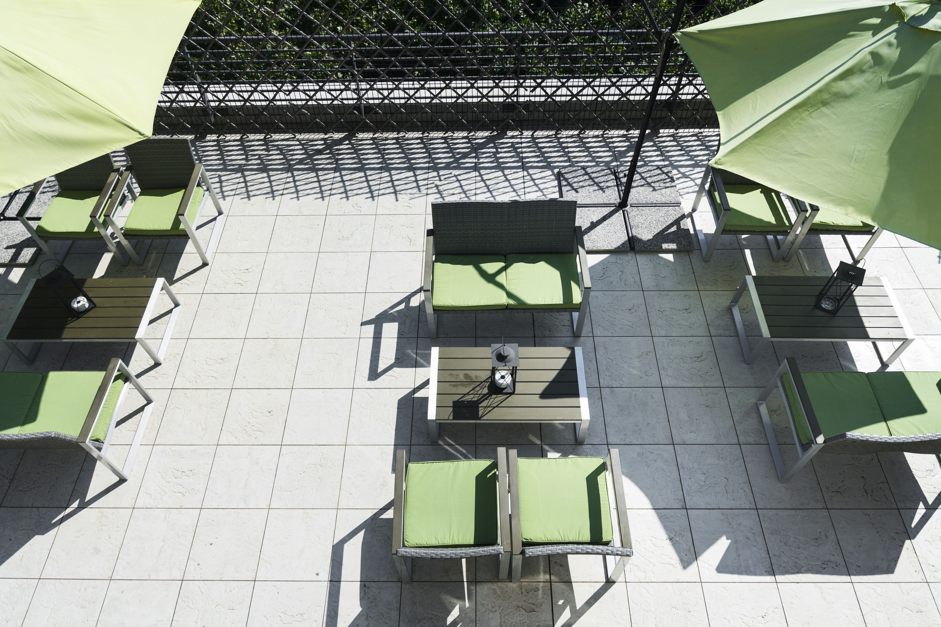 A patio area with outdoor seating including chairs and tables, a small table with a clock, and a green umbrella providing shade.