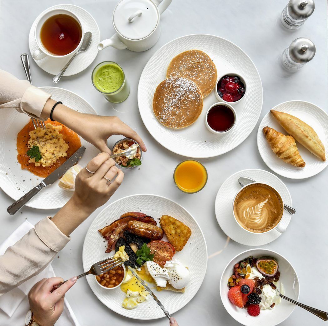 Ein Frühstückstisch mit verschiedenen Speisen, darunter Pfannkuchen, Eier, Würstchen und Gebäck.