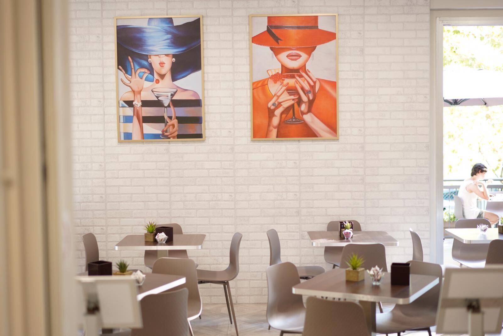 Uma sala de jantar moderna com paredes de tijolos brancos, duas obras de arte emolduradas e mobiliário contemporâneo.