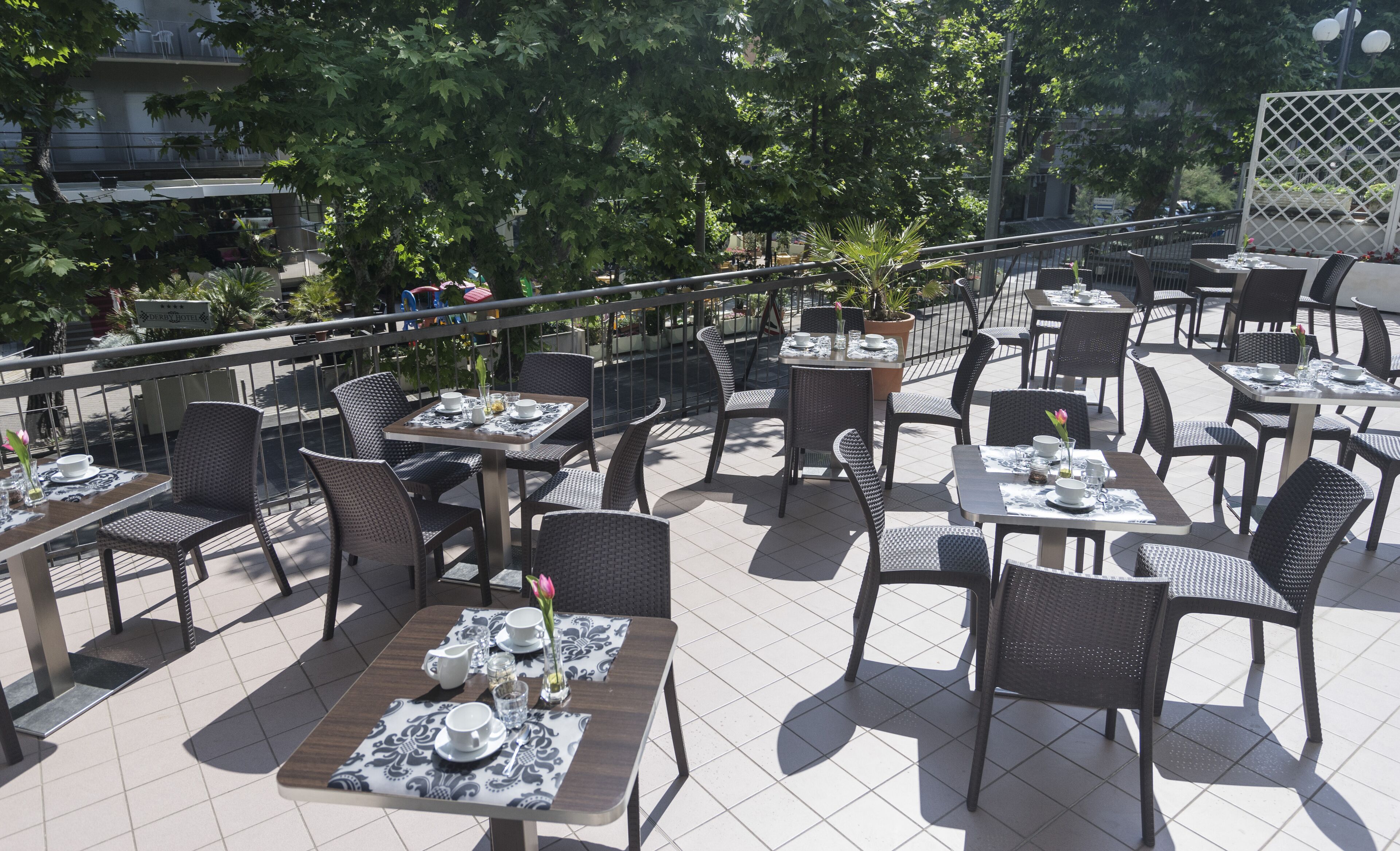 An outdoor café with tables and chairs, surrounded by trees and a railing.