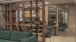 A modern interior with a green sofa, wooden shelves, and a bar area with chairs and tables. - Club Meeting Hotel (Rimini)