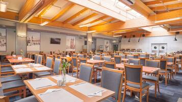 A spacious dining area with multiple tables and chairs, wooden beams on the ceiling, and artwork on the walls.