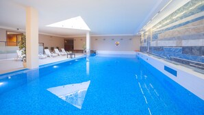An indoor swimming pool with clear blue water, lounge chairs, and a skylight. - Express Kraków Hotel (Kraków)