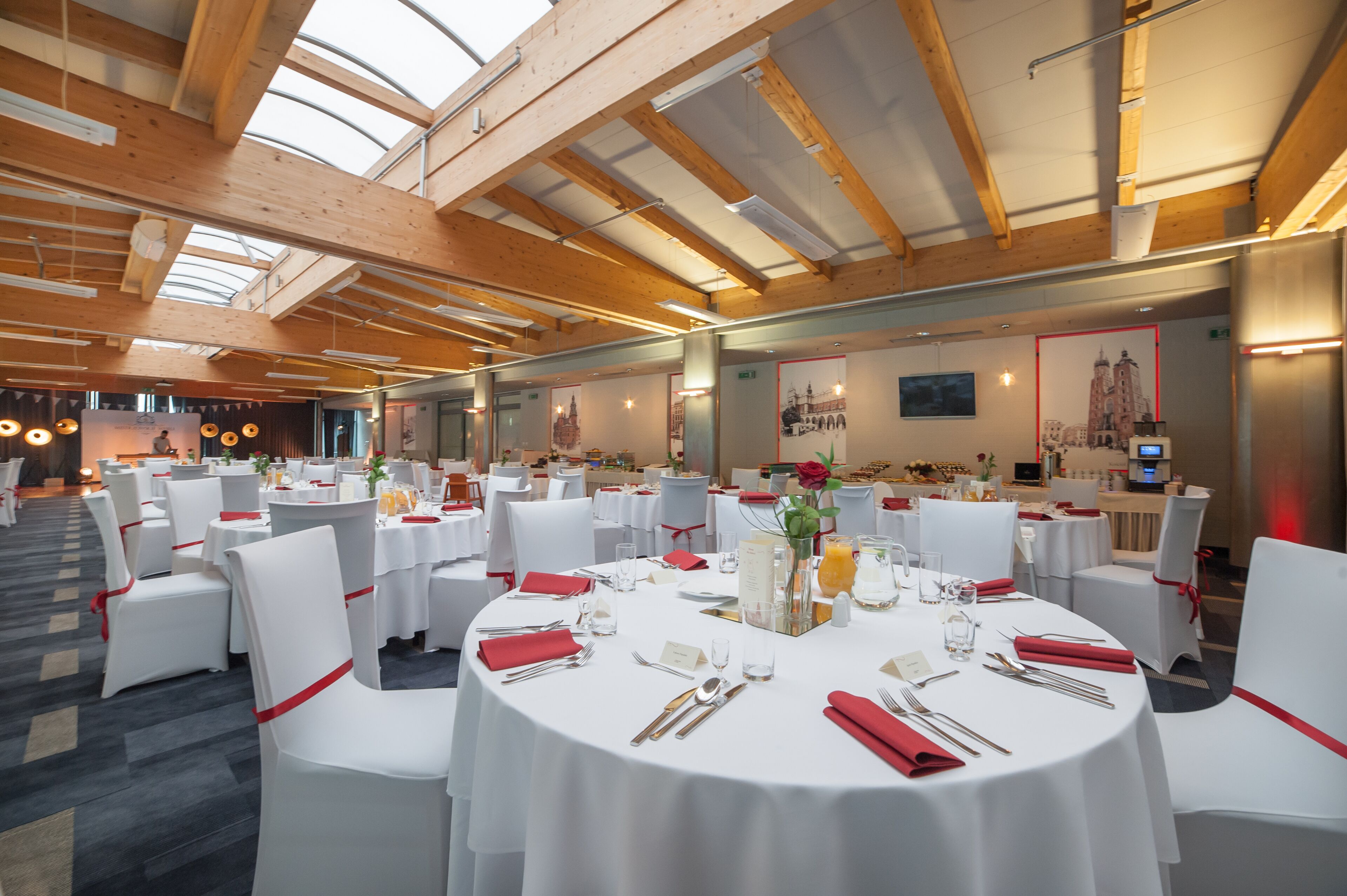 Une salle de banquet avec des tables rondes dressées pour le repas, des chaises blanches et des rubans rouges.