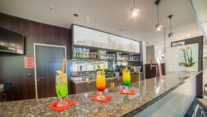 A bar area with a granite countertop, multiple bottles, and three colorful drinks. - Express Kraków Hotel (Kraków)