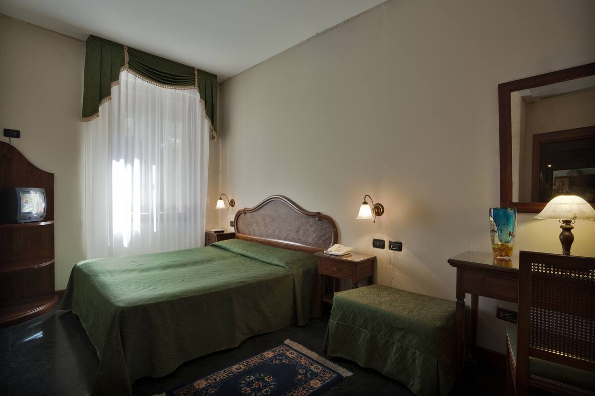 Una habitación de hotel con dos camas, un escritorio, una silla, un televisor y una lámpara.