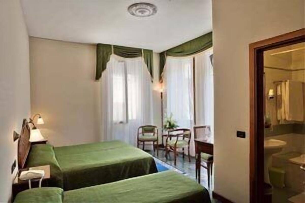 Una habitación de hotel pequeña con dos camas individuales, un escritorio y una silla.
