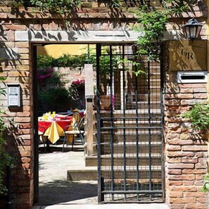 Une entrée en pierre, avec un portail en métal, un escalier menant à l’intérieur et une table recouverte d’une nappe jaune à l’extérieur.