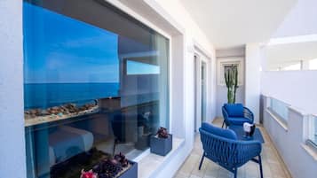 Un balcon avec vue sur la mer, un coin salon avec une table et des chaises, et une plante en pot.