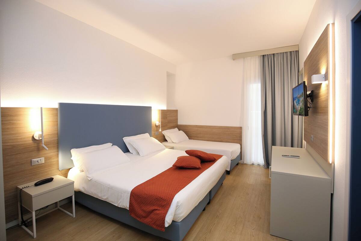 A hotel room with two beds, a desk, a TV, and a minibar.