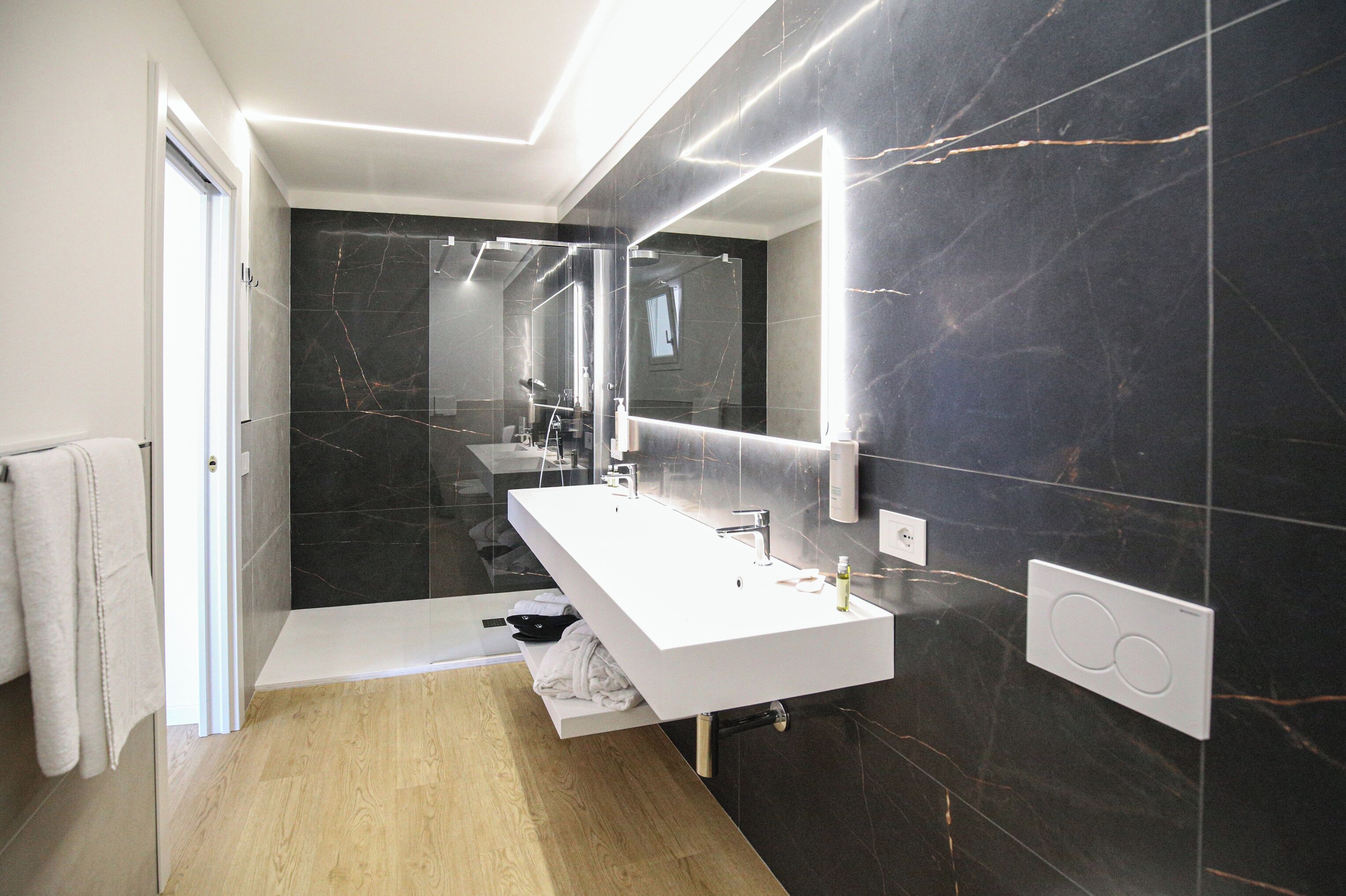 A modern bathroom with a large mirror, a white sink, and dark marble walls.