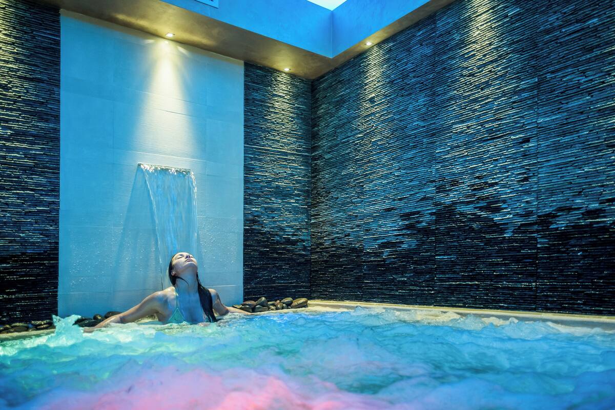 A modern spa with a large hot tub, a glass curtain, and a textured wall.